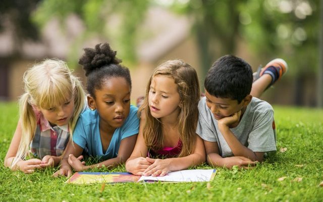 4 kids reading a book on the green