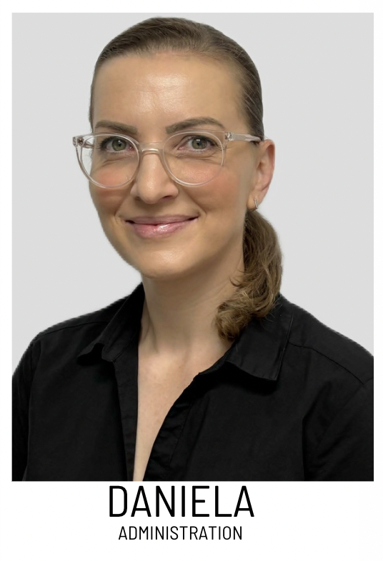 Portrait of Daniela, administrator, smiling in a black shirt and clear glasses, against a light background
